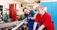 Zwei Personen bei der Arbeit Zwei Männer arbeiten gemeinsam an einer Maschine in einer Werkstatt.