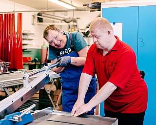 Zwei Personen bei der Arbeit Zwei Männer arbeiten gemeinsam an einer Maschine in einer Werkstatt.